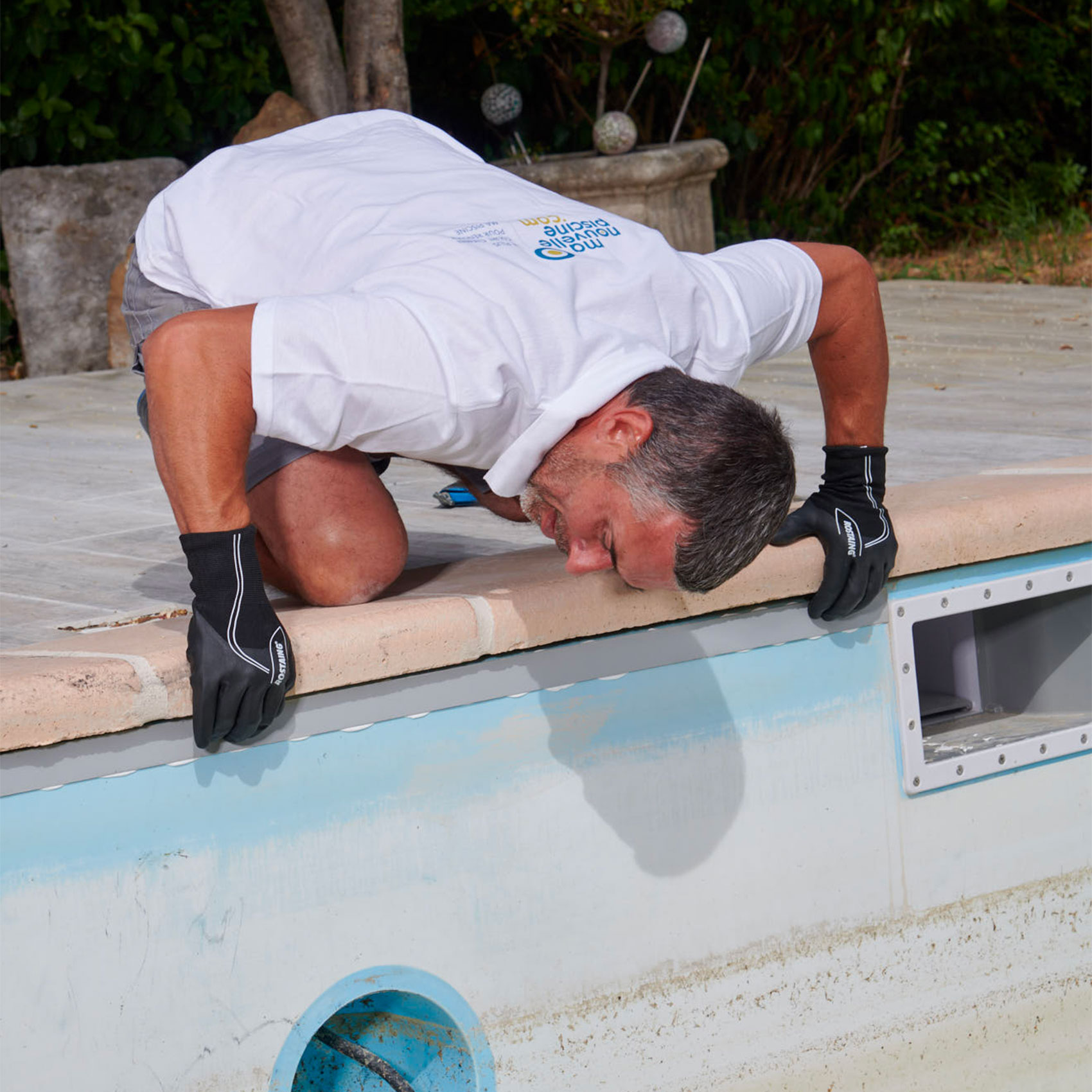 Description pour la balise alt : "Homme en chemise blanche travaillant sur la maintenance d'une piscine, examinant l'intérieur à travers une ouverture."
