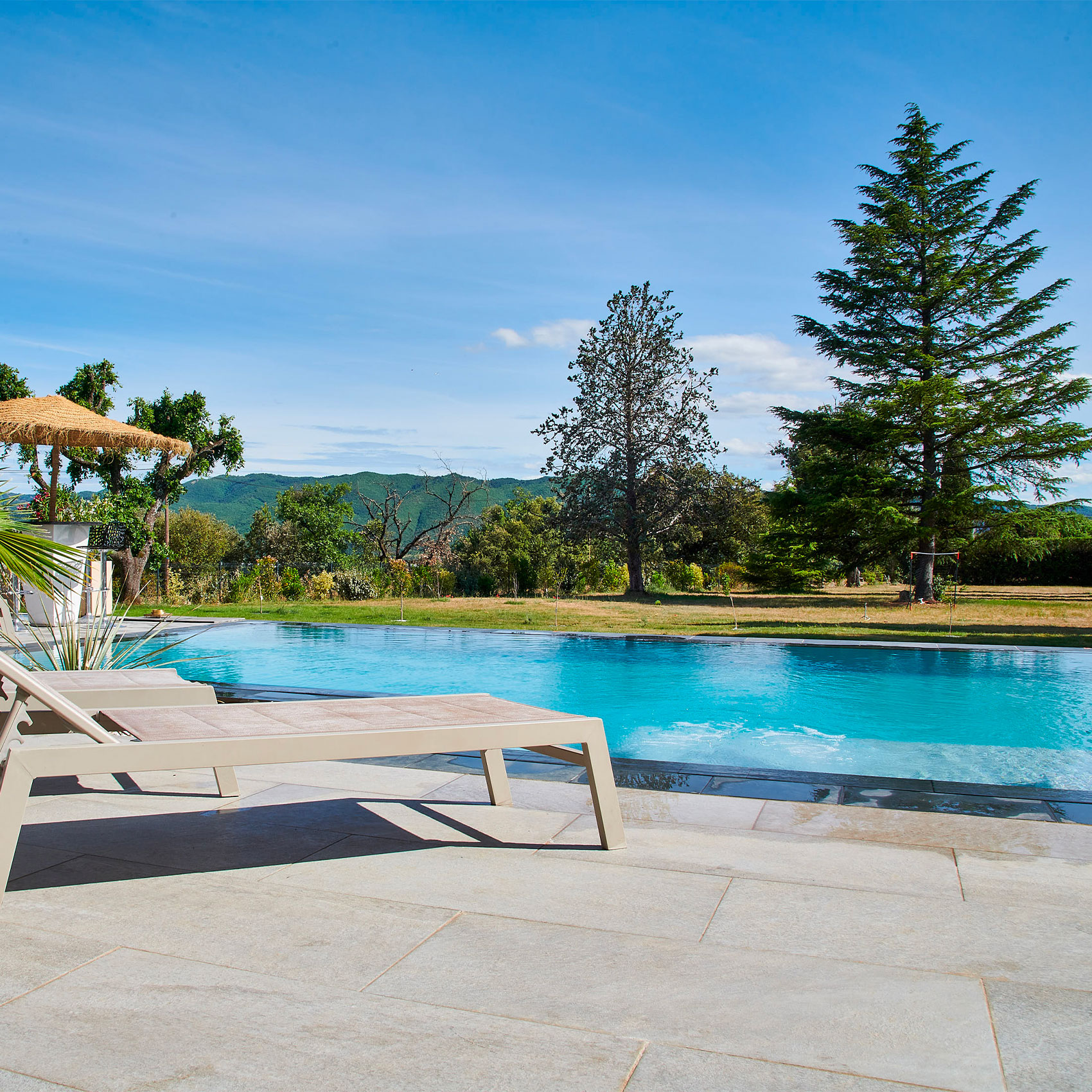 Piscine extérieure luxueuse avec chaises longues et vue sur les montagnes et la nature verdoyante.