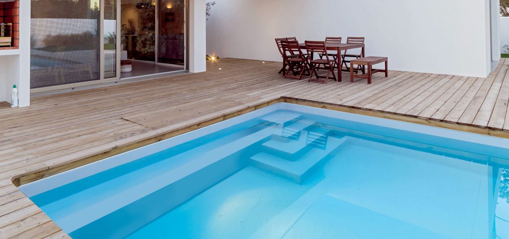Terrasse moderne en bois avec mobilier d'extérieur et piscine lumineuse dans une maison contemporaine.