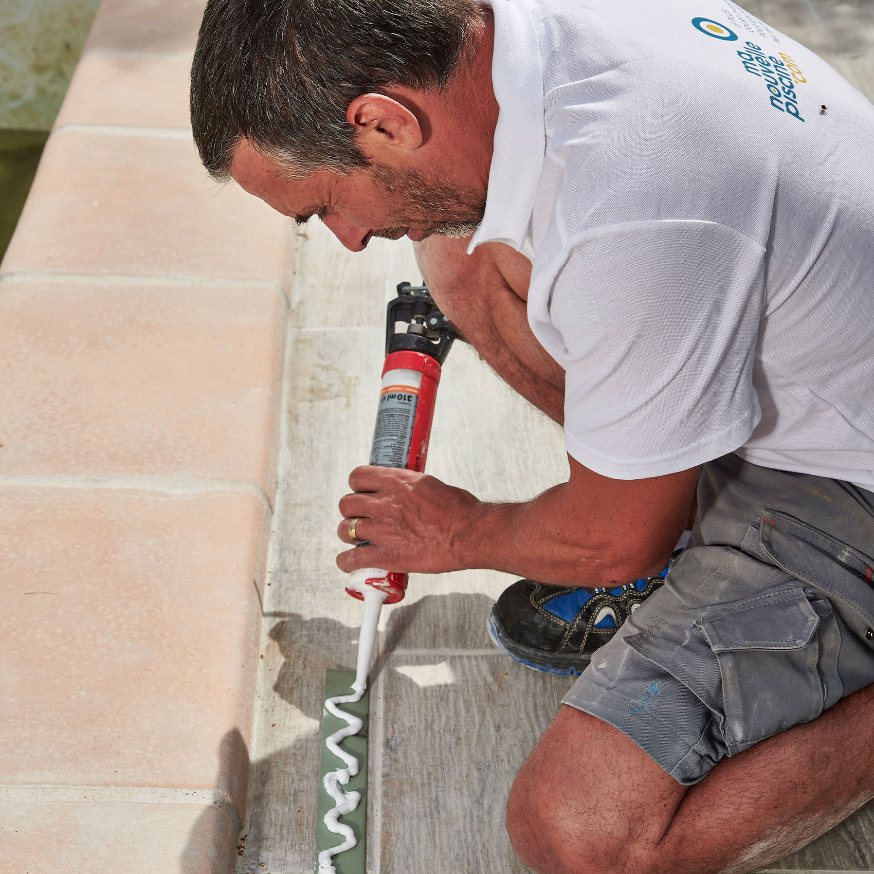 Homme appliquant du mastic avec un pistolet à calfeutrer sur des joints de carrelage extérieurs.